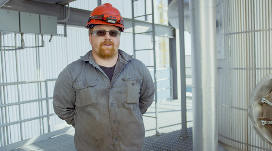 Wearing a red hardhat, American Crystal Sugar house mechanic, Will Hunt smiles as he stands in the Crystal Sugar factory